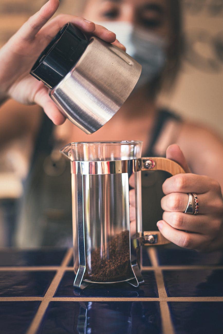 photo of person holding stainless cup pouring ground coffee on french press